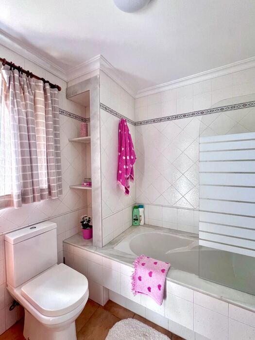 Baño con bañera, mampara y estantes de obra
