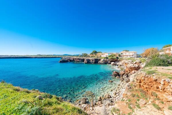 Cala de aguas turquesa entre rocas y acantilado con casas